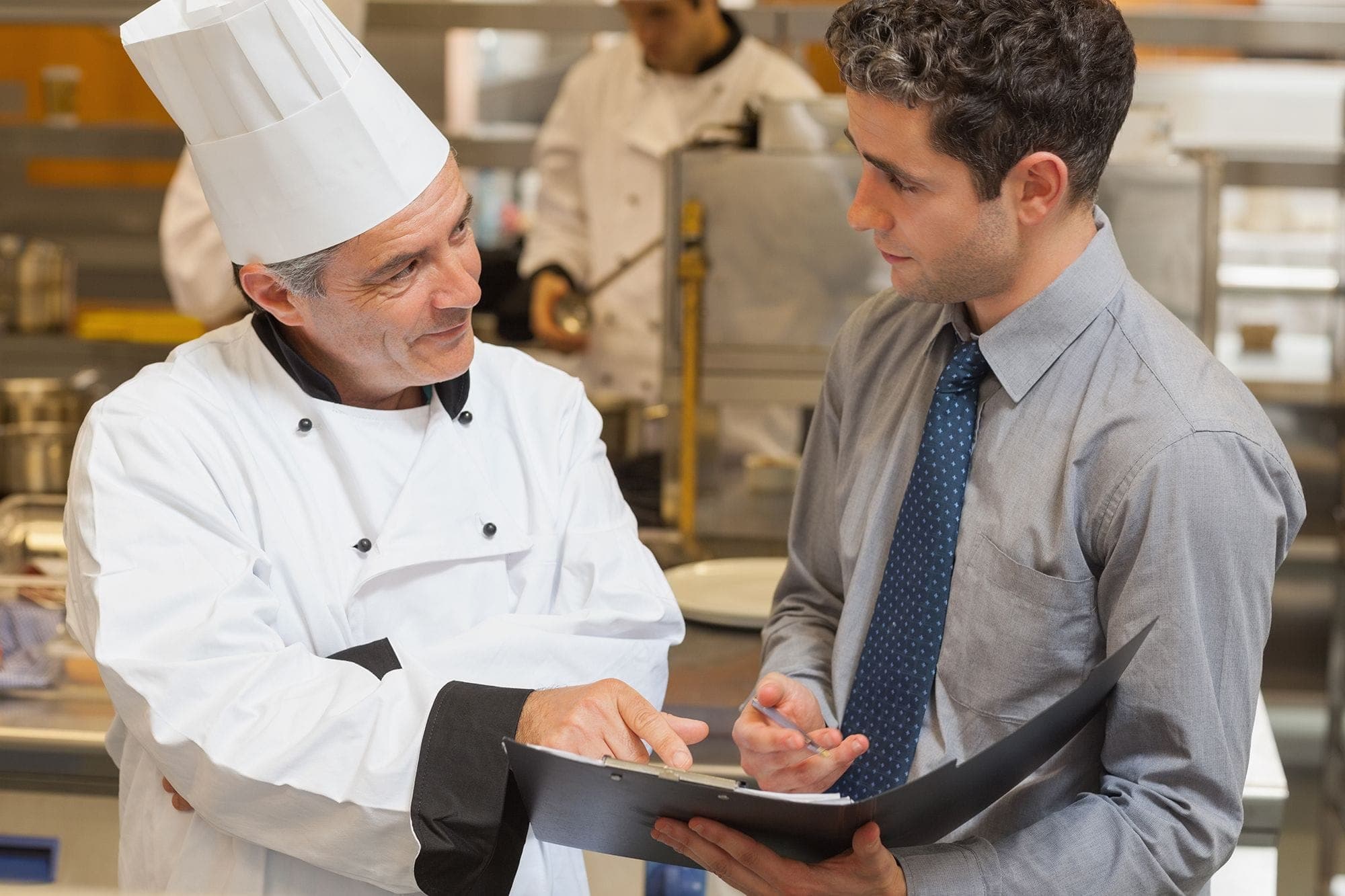 Photograph of a franchise operator chatting with a restaurant employee. The operator has a laptop open and is reviewing information on it with the employee.