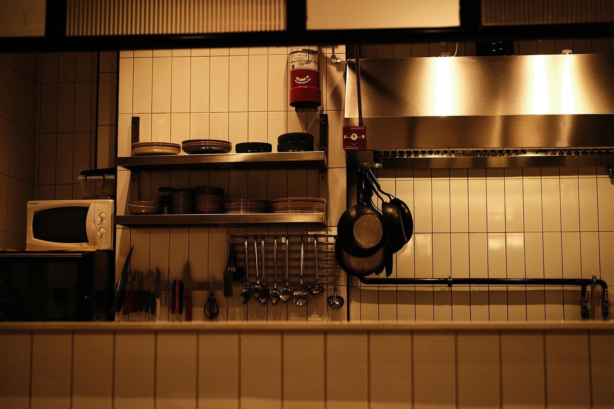 Photograph of a commercial kitchen with a fire extinguisher mounted on the wall above the prep shelves.
