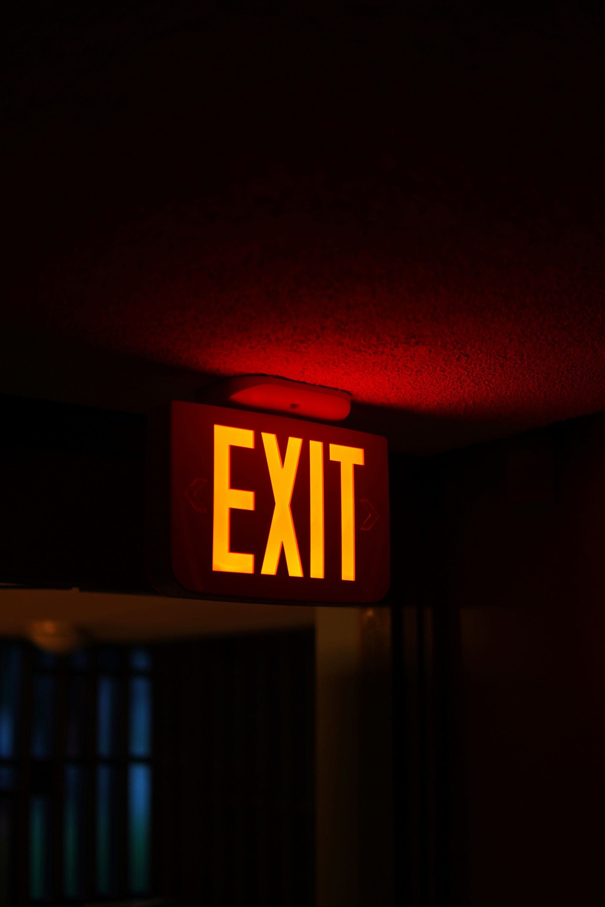 Photograph of an exit sign brightly lighting up in a dark hallway.