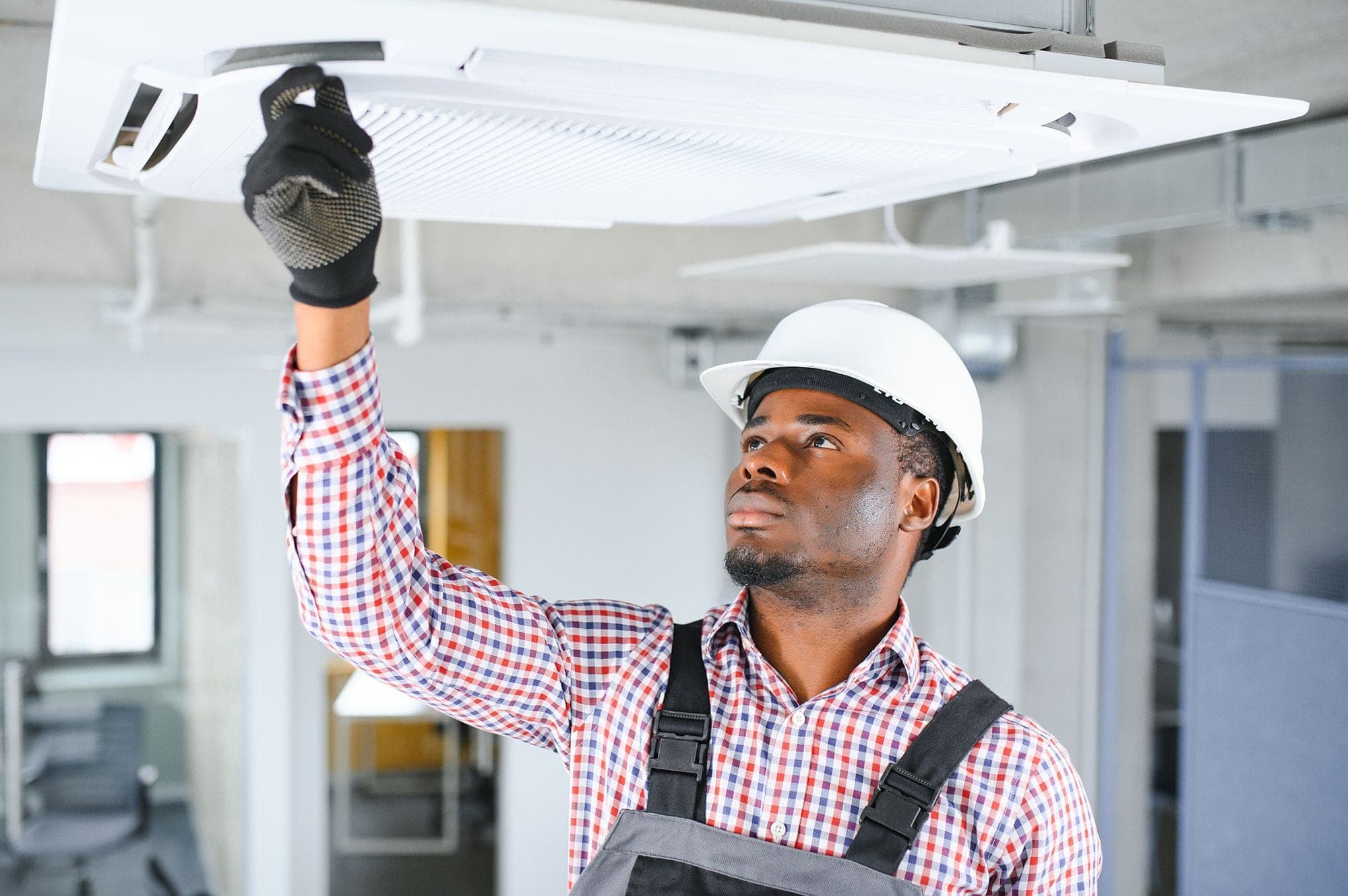 Photograph of an inspector reaching up to check the battery box of an emergency lighting system.