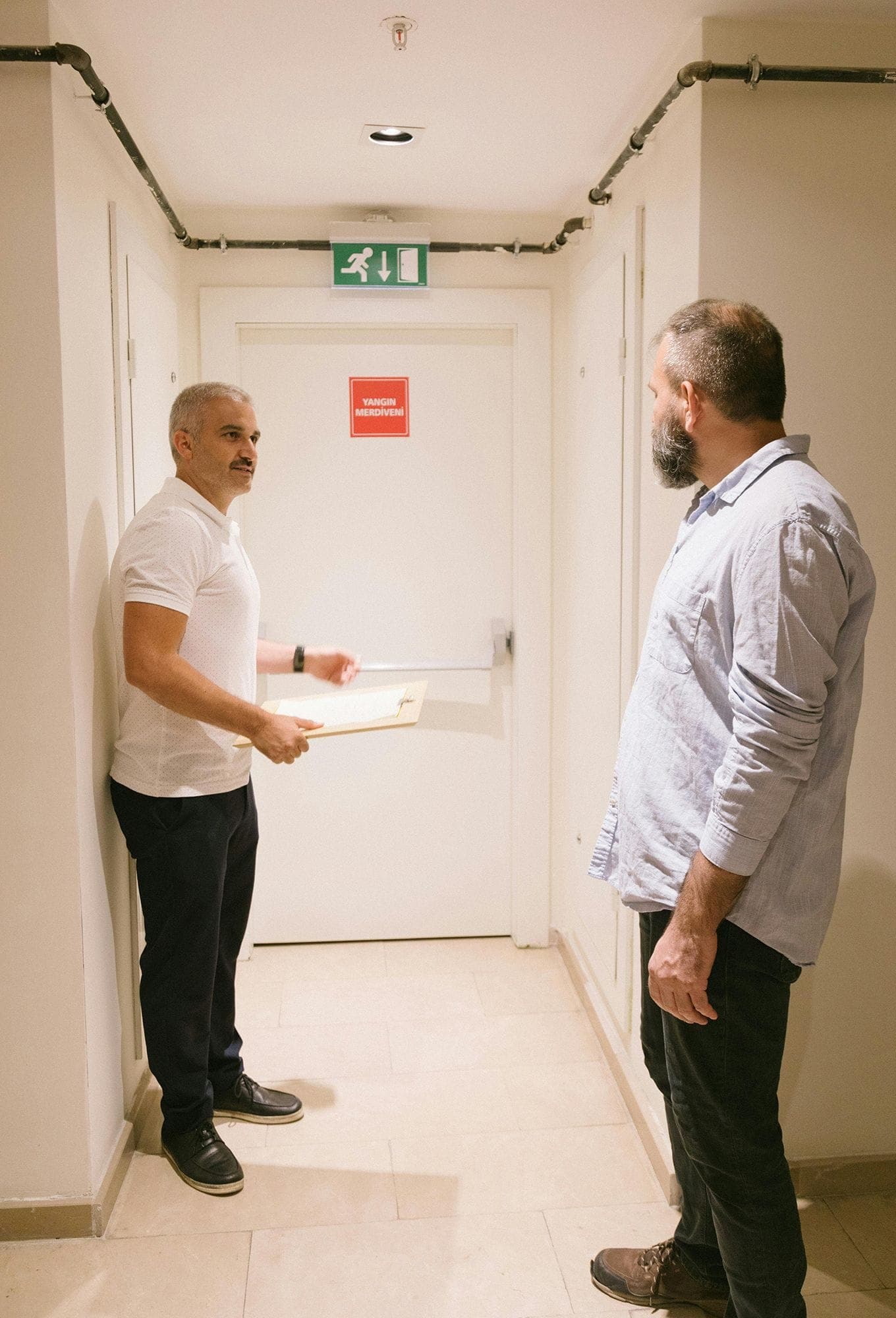 Photograph of a facility manager, holding a clipboard, showing a location's emergency exit route to a client.